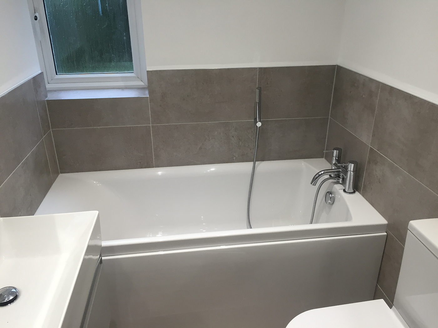 Bath with a shower screen and large grey wall tiles