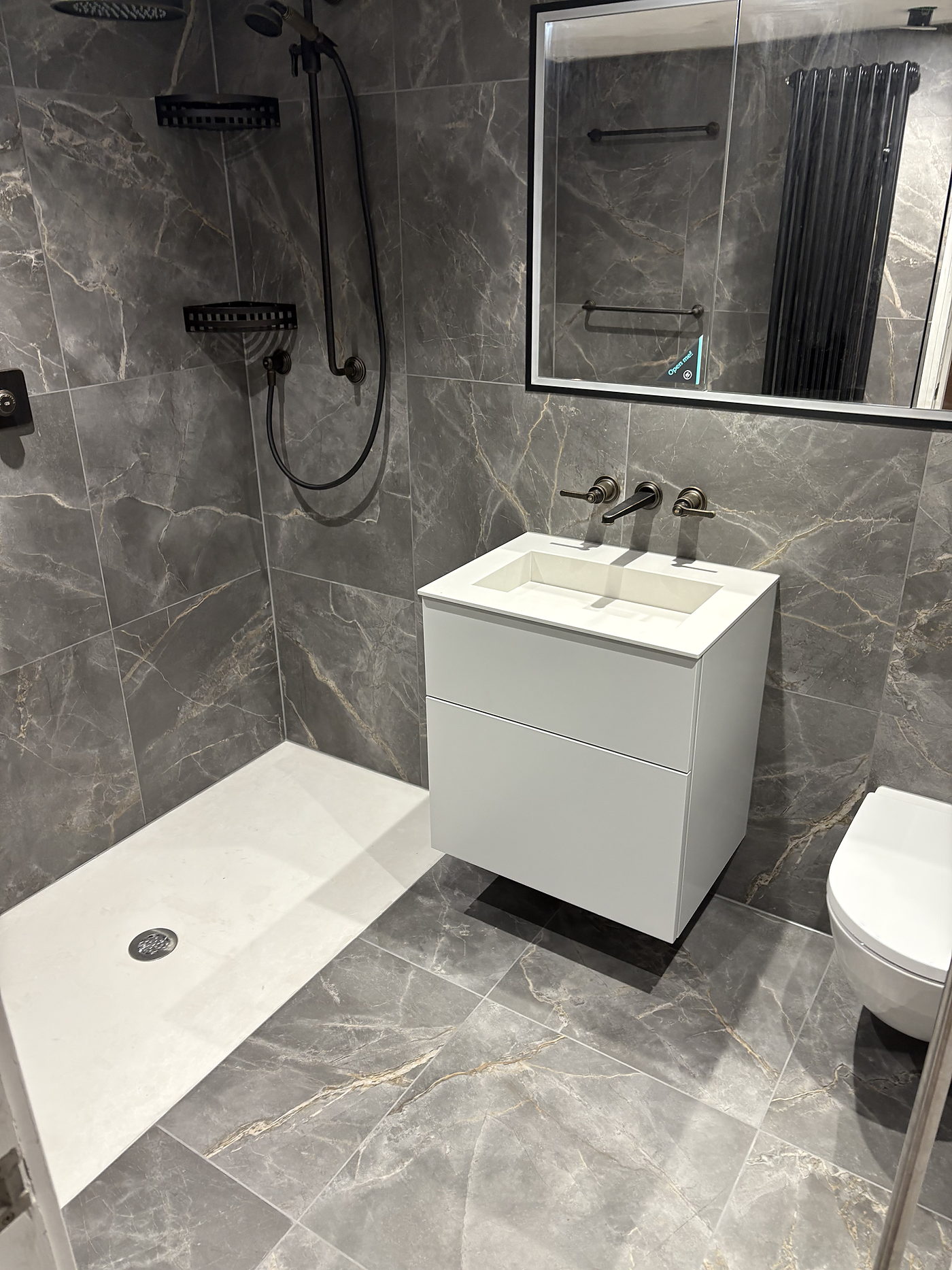 Walk in shower and wall hung basin unit in a dark marble tiled bathroom