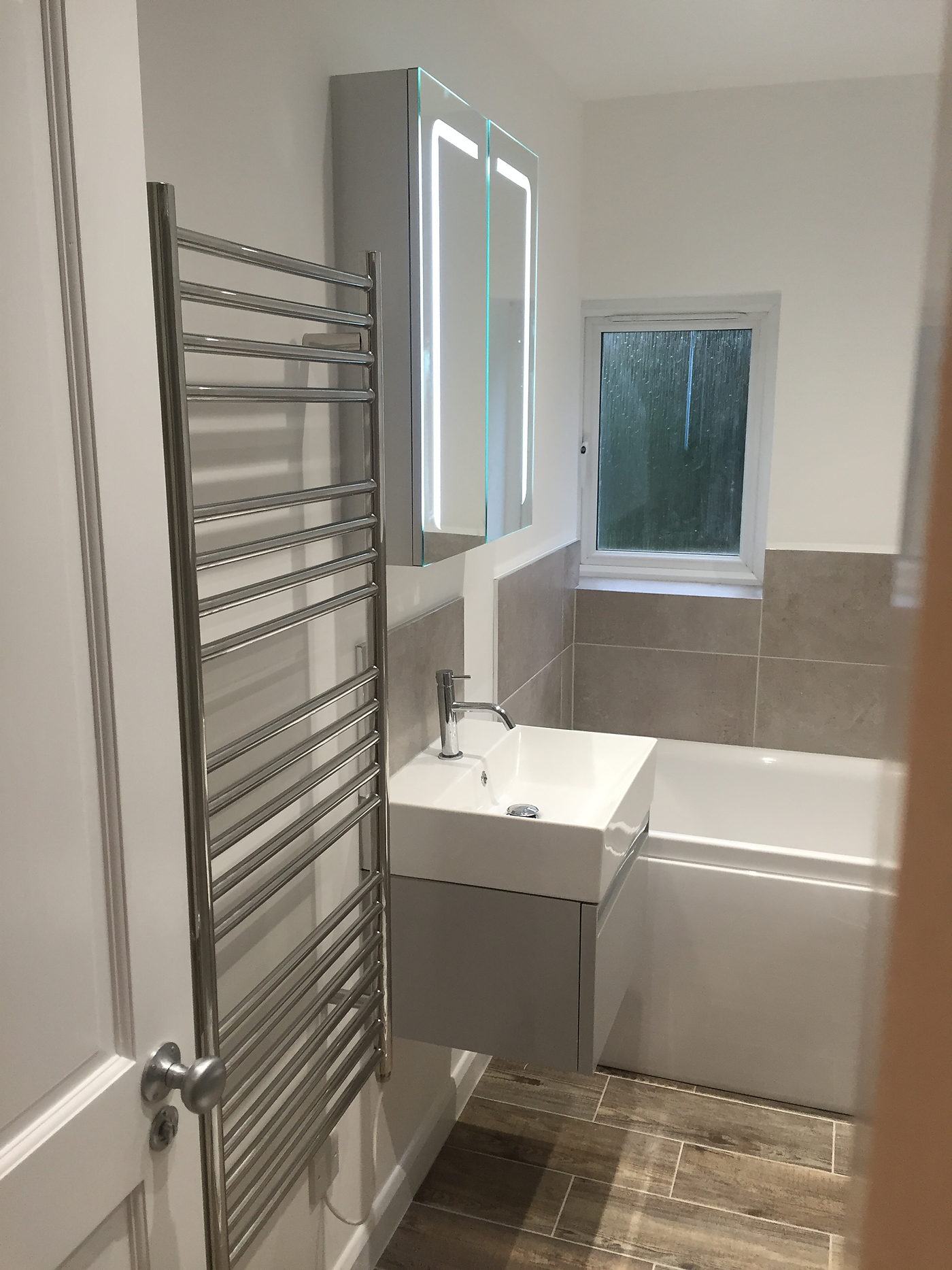Basin unit, heated towel rail and a backlit mirror in a finished bathroom