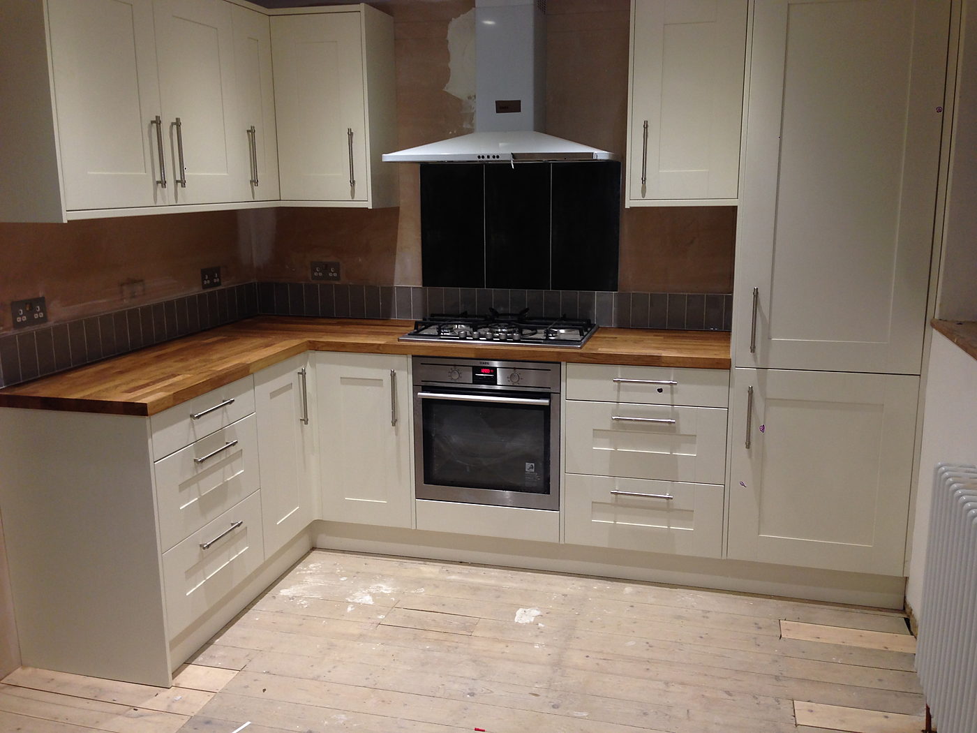 Cream kitchen with a black glass splashback, built in oven and downlights