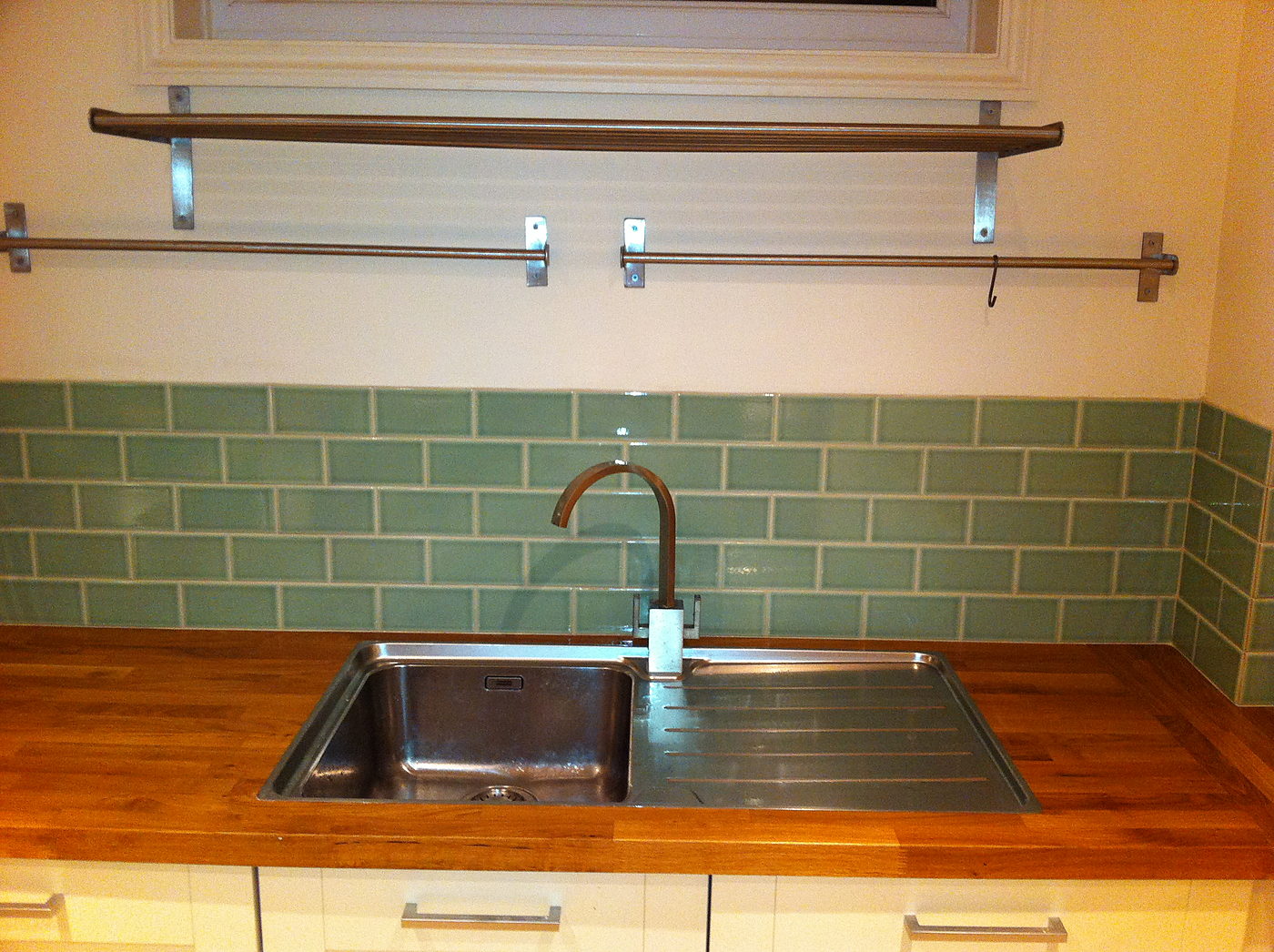 Kitchen sink set into an oak worktop with a green tiled splashback
